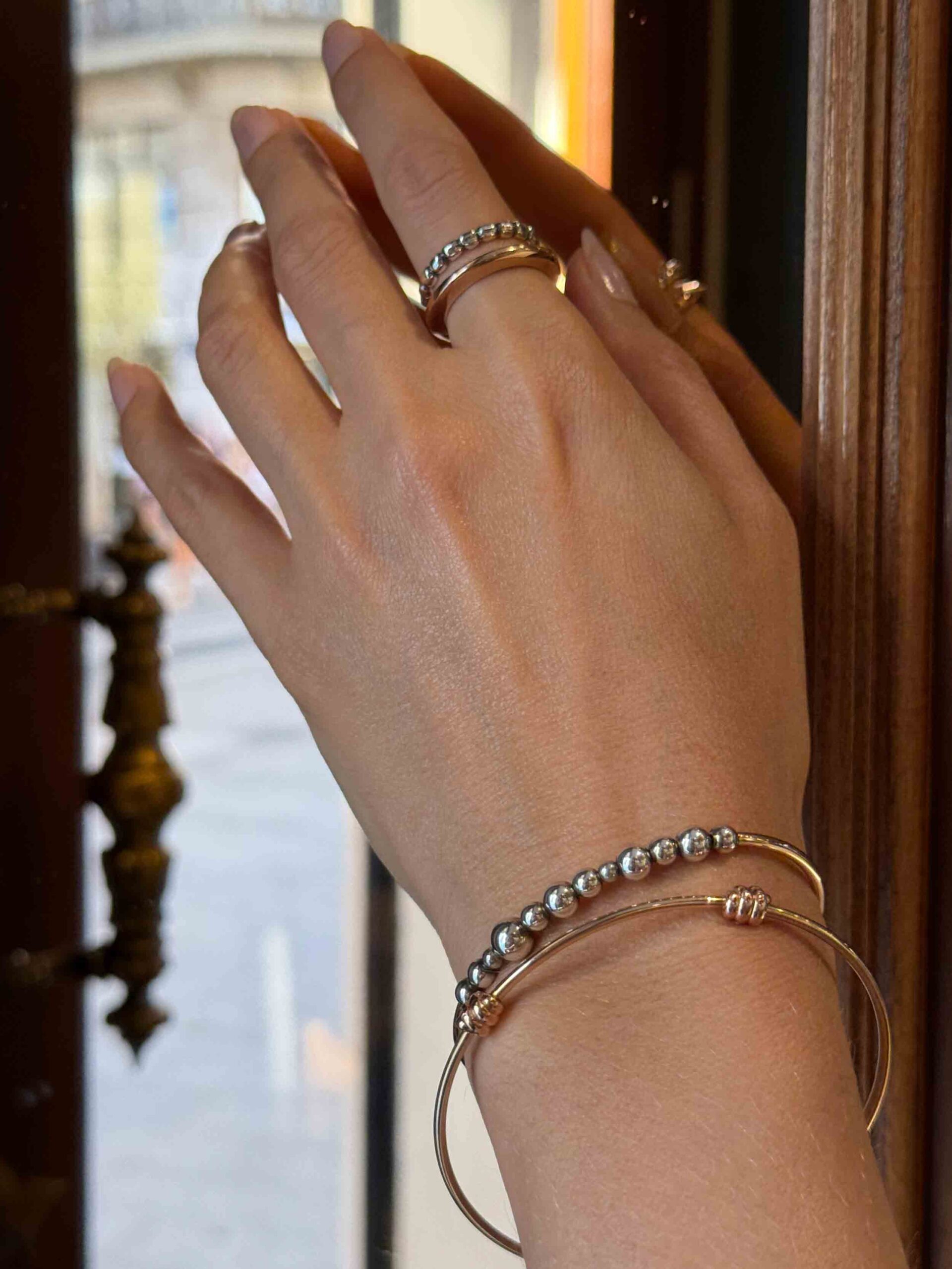 Mano de mujer con dos pulseras y dos anillos que son de oro rosa y de plata, que simbolizan la tendencia de mezclar varios metales.