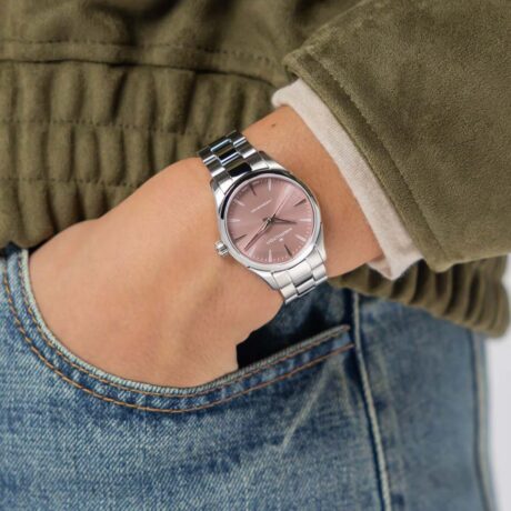 El Hamilton Jazzmaster Quartz 32 mm H32301171 es una elegante reinterpretación de un clásico reloj de vestir, diseñado para quienes buscan una pieza sofisticada, femenina y atemporal con un toque contemporáneo. Su delicada esfera en color rosa empolvado, con acabado cepillado de efecto rayos de sol, aporta luminosidad y profundidad al diseño. Las refinadas agujas esqueletizadas tipo dauphine realzan su carácter elegante, mientras que los detalles pulidos de la caja aportan un aspecto distinguido y moderno. La caja de acero inoxidable de 32 mm presenta una silueta equilibrada y especialmente cómoda gracias a su perfil ultraplana de tan solo 7,8 mm de grosor. El cristal de zafiro con tratamiento antirreflejos protege la esfera y garantiza una excelente legibilidad, además de una gran resistencia a los arañazos. En su interior incorpora el calibre de cuarzo F05.105, un movimiento suizo fiable y preciso que ofrece la comodidad de un mantenimiento reducido y una excelente exactitud en el día a día. Con una resistencia al agua de 5 bares (50 metros), el Jazzmaster Quartz está preparado para acompañarte en cualquier ocasión, desde los compromisos diarios hasta los eventos más especiales. El Hamilton Jazzmaster Quartz 32 mm combina la frescura de un diseño actual con la elegancia clásica que define la colección Jazzmaster, convirtiéndose en una opción perfecta para quienes valoran la sofisticación discreta y el estilo atemporal. Referencia Hamilton: H32301171 Referencia interna: 000010773