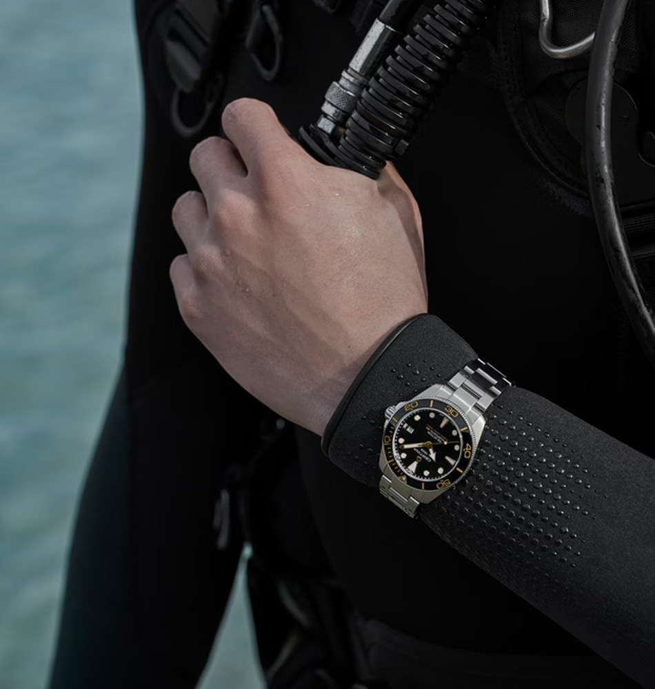 El Certina DS Action Diver 40,5 mm Powermatic 80, referencia C048.407.11.051.01, es un reloj diseñado para el submarinismo profesional, que combina robustez, precisión y una estética deportiva y sofisticada. Su caja y brazalete están fabricados en acero inoxidable 316L, mientras que el bisel combina acero inoxidable 316L y un inserto de cerámica. Su esfera negra incorpora detalles con Super-LumiNova®, proporcionando una excelente legibilidad incluso en condiciones de poca luz. Cuenta con un cristal de zafiro con tratamiento antirreflectante en una sola cara, ofreciendo una elevada resistencia a los arañazos y una óptima lectura de la esfera. Con una hermeticidad de hasta 300 metros, cumple la norma ISO 6425:2018, que establece los requisitos para los relojes de submarinismo profesionales. Sus dimensiones de 40,5 mm de diámetro, 14,1 mm de altura, 20 mm entre asas y 48,3 mm de longitud entre asas proporcionan una presencia equilibrada en la muñeca. En su interior incorpora el calibre automático Powermatic 80.611, con una impresionante reserva de marcha de hasta 80 horas y espiral Nivachron™, diseñada para ofrecer una mayor resistencia frente a los campos magnéticos. Además, este modelo incorpora el New DS Concept Extreme Shock Resistance, una evolución del sistema de protección DS de Certina desarrollada para incrementar la resistencia del reloj frente a impactos y condiciones exigentes. Referencia Certina: C048.407.11.051.01 Referencia interna: R-CER-DS1-0006