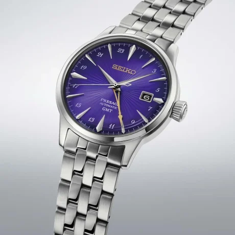 El Seiko Presage Cocktail Time Seiko 145th Anniversary Limited Edition HCB006 celebra el 145.º aniversario de Seiko con una edición limitada a 6.000 piezas. Su esfera púrpura con patrón radial, característica de la colección Cocktail Time, se inspira en el cóctel «Edo Murasaki», creado en colaboración con Hisashi Kishi, propietario de STAR BAR. Esta tonalidad evoca el patrimonio cultural de Tokio y su evolución a lo largo del tiempo, mientras que el logotipo y la aguja GMT en tono dorado aportan un contraste elegante y simbolizan un futuro brillante. En su interior incorpora el calibre automático 4R34, un movimiento mecánico con capacidad de carga manual, 24 rubíes y una reserva de marcha aproximada de 41 horas. La aguja de 24 horas permite consultar un segundo huso horario, mientras que la función de parada del segundero facilita un ajuste preciso de la hora. También dispone de visualización de la fecha. La caja de acero inoxidable de 40,5 mm incorpora un cristal Hardlex con forma de caja y un fondo transparente y roscado que permite contemplar el movimiento mecánico. El conjunto se completa con un brazalete de acero inoxidable y un cierre desplegable con botón de apertura. Su resistencia al agua de 5 bares y su resistencia magnética de 4.800 A/m completan sus características técnicas. El Seiko Presage Cocktail Time Seiko 145th Anniversary Limited Edition HCB006 combina la tradición relojera japonesa con una esfera de inspiración coctelera y la funcionalidad GMT, en una edición conmemorativa cuyo fondo de caja incorpora la inscripción «LIMITED EDITION». Descubre toda nuestra colección de relojes Seiko. Referencia Seiko: HCB006 Referencia interna: R-SEI-PRE-0020
