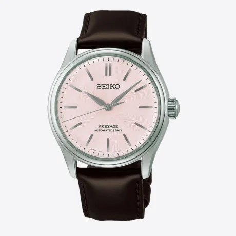 El Seiko Presage Classic Series Sakura Iro HCC003J1 captura la esencia de una de las estampas más emblemáticas de Japón a través de una elegante interpretación de los cerezos en flor. Su delicada esfera rosa sakura-iro evoca los suaves tonos de los pétalos de sakura, mientras que la correa de piel marrón oscuro, inspirada en el tronco del cerezo, aporta equilibrio y sofisticación al conjunto. En su interior incorpora el calibre automático 6R51, un movimiento mecánico de fabricación japonesa que ofrece una reserva de marcha de hasta 72 horas, garantizando precisión y fiabilidad durante varios días. Su diseño de tres agujas refleja la elegancia clásica característica de la colección Presage. La caja de acero inoxidable de 38 mm se combina con un cristal de zafiro de doble curvatura con tratamiento antirreflectante, que mejora la legibilidad y realza la belleza de la esfera. Además, cuenta con un fondo transparente roscado que permite admirar el movimiento automático, así como una resistencia al agua de 10 ATM (100 metros) para una mayor versatilidad en el uso diario. Referencia Seiko: HCC003J1 Referencia interna: R-SEI-PRE-0013
